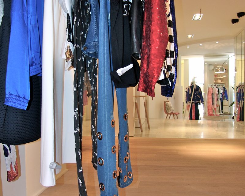 Hangende kleding in blauw, rood en zwart met laarzen, met de winkel op de achtergrond