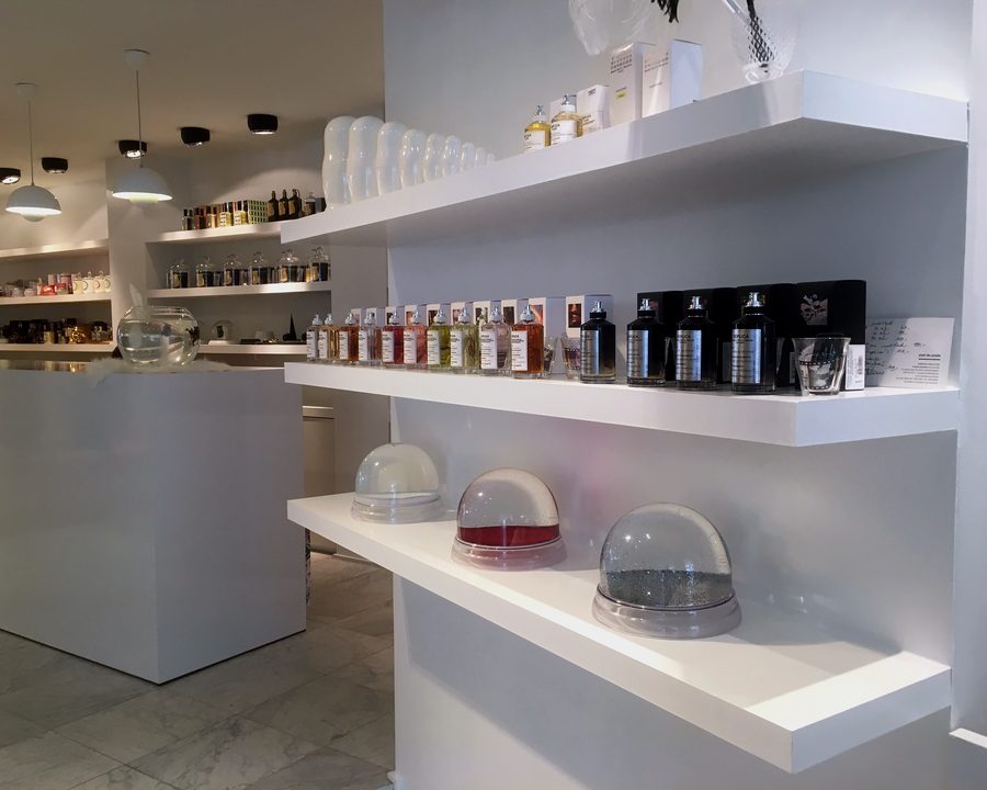 Parfumflessen op witte schappen in de winkel, met decoratieve glazen stolpen eronder